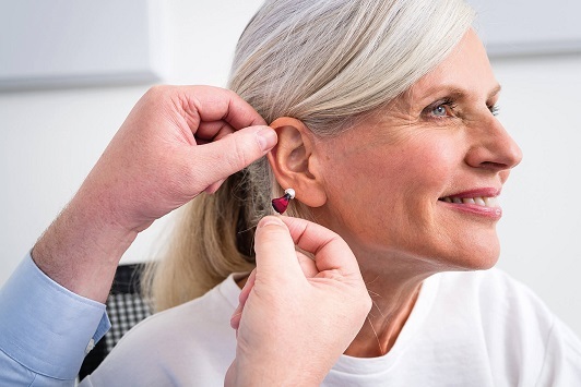 Seniorin mit grauen Haaren bekommt von einem Hörakustiker ein Hörgerät eingesetzt.